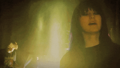 a woman singing in a dark room with a man playing a guitar