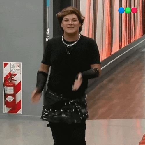 a woman in a black shirt is dancing in a hallway with a fire extinguisher in the background
