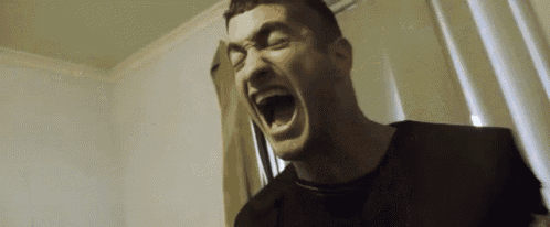 a man in a black shirt is screaming with his mouth open in a room .
