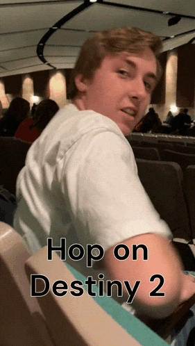 a man in a white shirt is sitting in an auditorium with the words hop on destiny 2 on the bottom