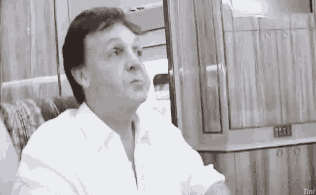 a man in a white shirt is sitting in a chair with tini written on the bottom right