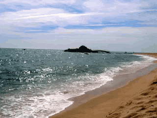 waves crashing on a sandy beach with a small island in the background