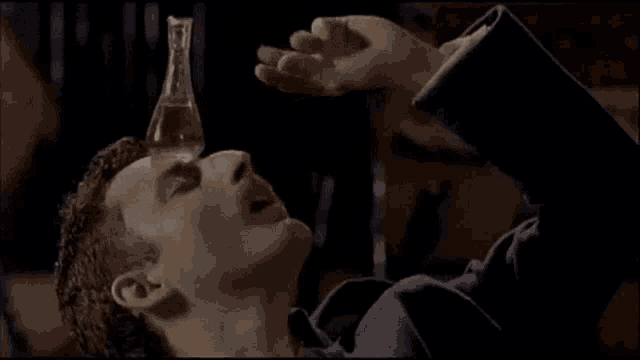 a man is drinking from a glass bottle with his mouth open .