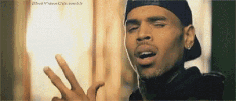 chris brown is wearing a hat and making a peace sign with his fingers .