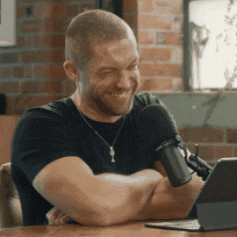 a man is smiling in front of a microphone while sitting at a table with his arms crossed