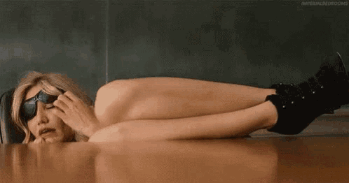 a naked woman is laying on a wooden floor with her legs crossed .