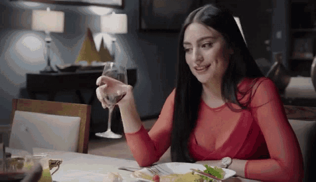 a woman in a red top holds a glass of wine
