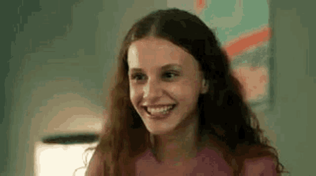 a young woman with long hair is smiling and looking at the camera in a room .