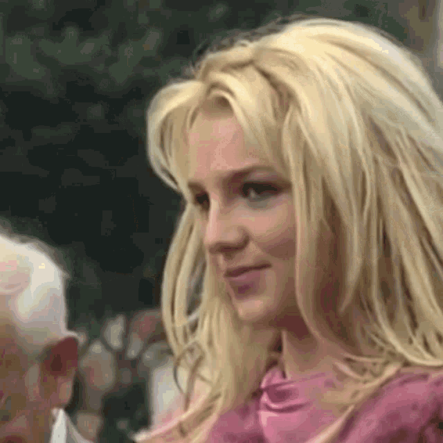 a close up of a blonde woman wearing a pink shirt and smiling .