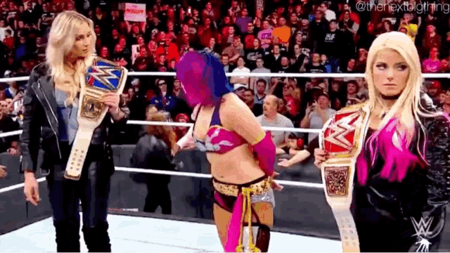 three female wrestlers are standing in a wrestling ring holding their championship belts .