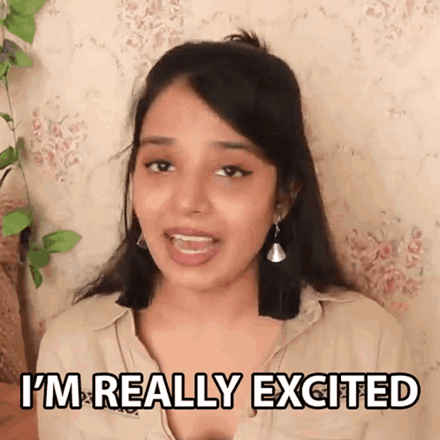 a woman is saying i 'm really excited in front of a floral wall .
