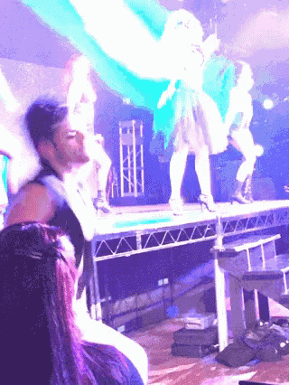 a group of people are dancing on a stage with purple lights
