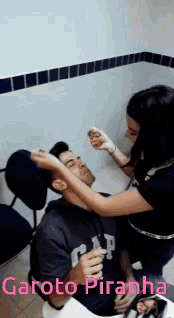 a girl is applying makeup to a man who is wearing a gap sweatshirt
