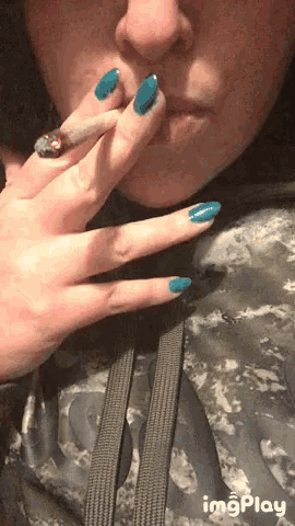 a woman with blue nails is smoking a cigarette while wearing a camouflage hoodie