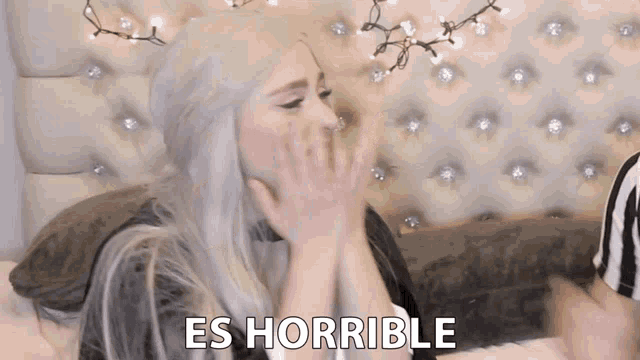 a woman with white hair is sitting on a bed with the words es horrible written on the bottom of her face .