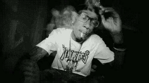 a black and white photo of a man smoking a cigarette while wearing glasses .