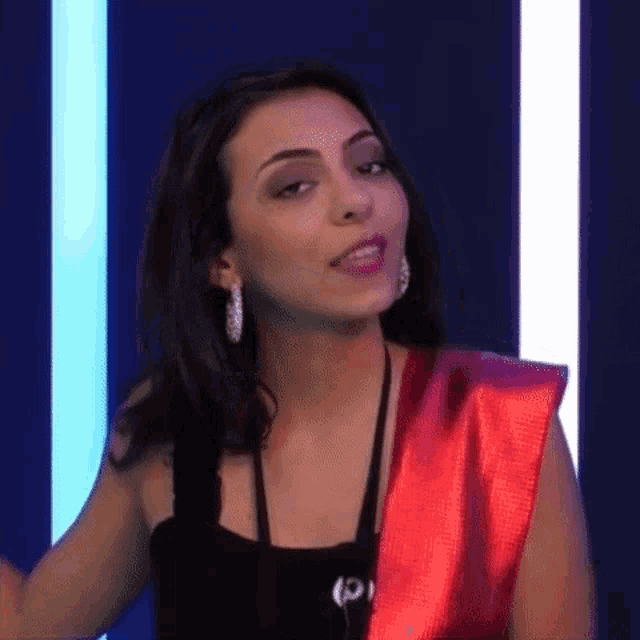 a woman wearing a black top and a red sash is standing in front of a blue background .