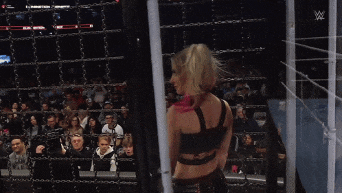 a woman stands behind a chain link fence in front of a crowd at a wrestling show