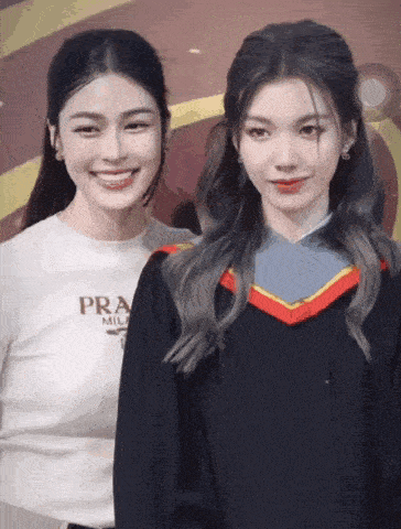 a woman wearing a prada shirt is standing next to a woman wearing a graduation gown