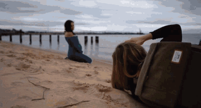 a person laying on a sandy beach with a herschel bag