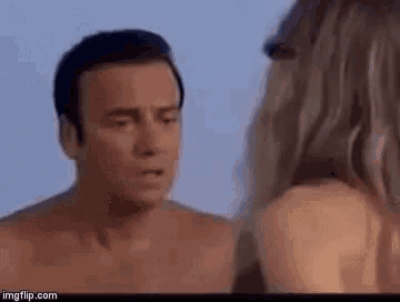 a shirtless man is standing next to a woman on a beach .