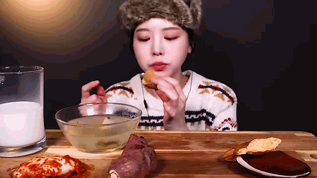 a woman is sitting at a table eating a sandwich and drinking milk .