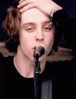 a young man is singing into a microphone while holding his hand to his forehead .