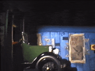 a green car is parked in front of a blue wall with a sign on it that says now play