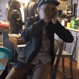a man wearing a hat that says ' coca cola ' on it is sitting in a kitchen