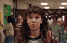 a girl with a backpack is standing in a hallway with a crowd of people .