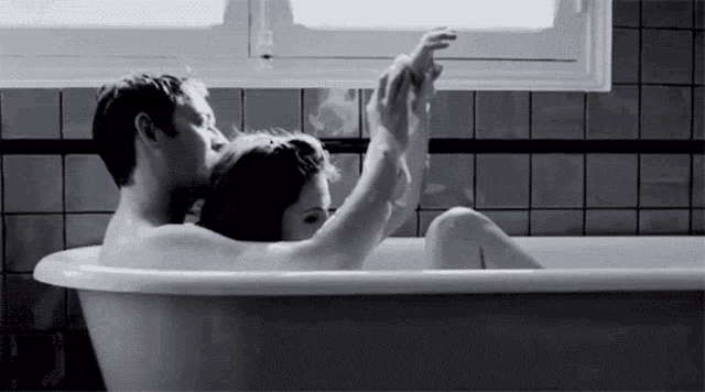 a man and woman are taking a bath together in a bathtub .