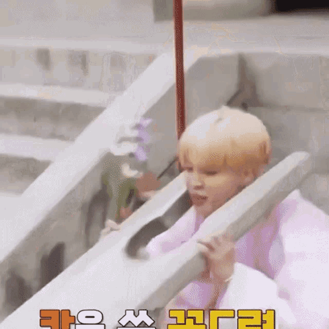 a man in a pink robe is sitting on a set of stairs holding a wooden stick .
