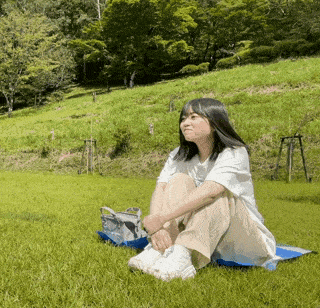 a woman is sitting on a blue blanket in the grass
