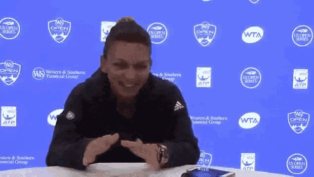 a woman sitting at a table in front of a wall that has wta logos on it