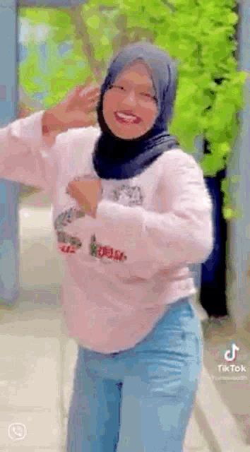 a woman wearing a hijab and a pink sweater is dancing in a video .