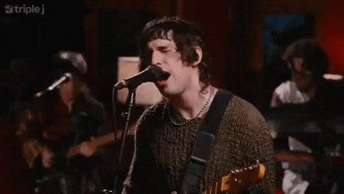 a man is singing into a microphone while playing a guitar in front of a group of people .