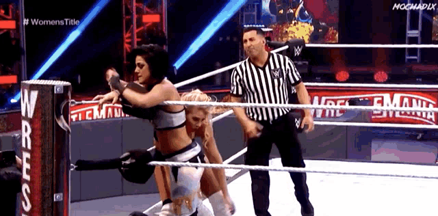 two women are wrestling in a ring while a referee watches