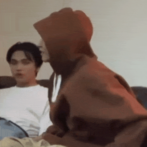 a man in a hoodie is sitting on a couch next to a man in a white shirt .