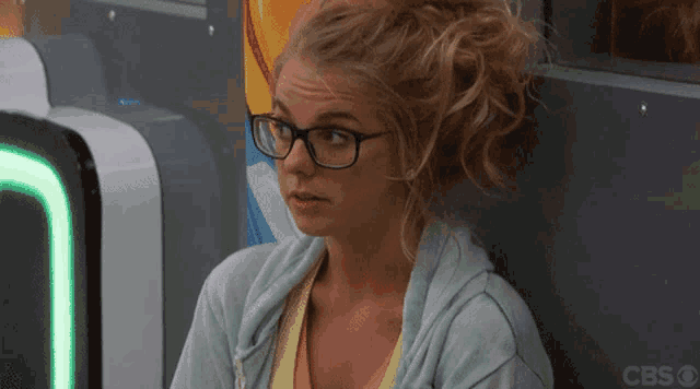 a woman wearing glasses sits in front of a cbs sign