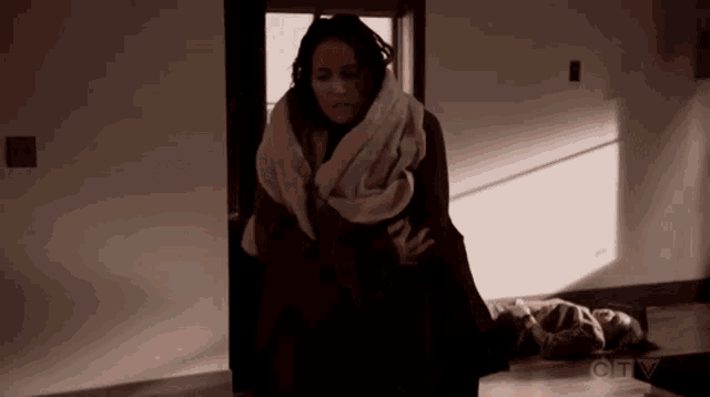 a woman wrapped in a blanket is standing next to a man laying on the floor ..