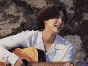 a man in a white shirt is holding a guitar and smiling