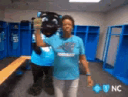 a woman is standing in a locker room with a mascot