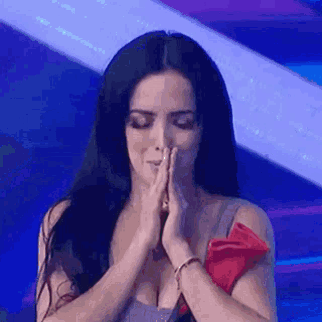 a woman with long black hair is praying with her hands folded in front of her face .