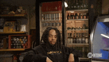 a man with dreadlocks is sitting in front of a fridge that says showtime on it
