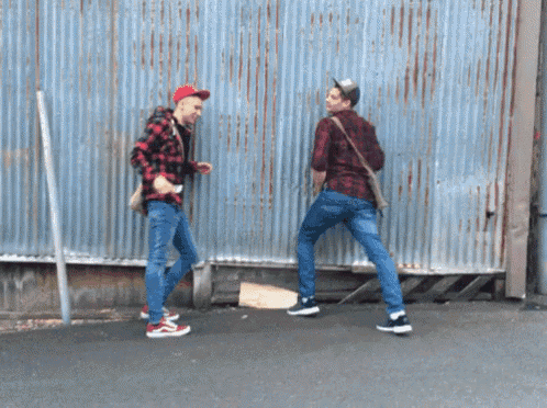 two men standing next to each other in front of a wall