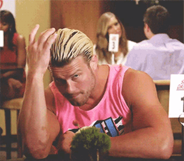 a man in a pink tank top sitting at a table
