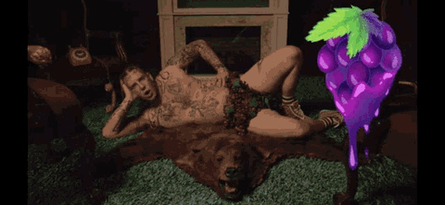 a tattooed man laying on a bear rug next to a purple grape with green leaves