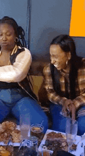 two women are sitting at a table with food and drinks and laughing .