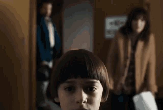 a young boy with a bob hairstyle is standing in front of a woman and a man .