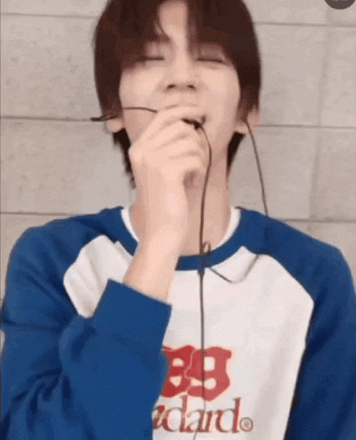a young man is singing into a microphone while wearing headphones and a blue shirt .